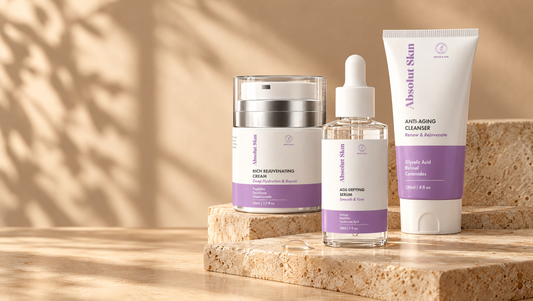 Absolut Skin Age-Defying Serum with the Rich Rejuvenating Cream and Anti-Aging Cleanser on warm travertine stone in soft window light.